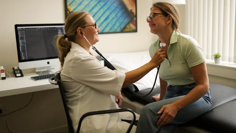 An advanced clinical practitioner examining a patient in a consultation room