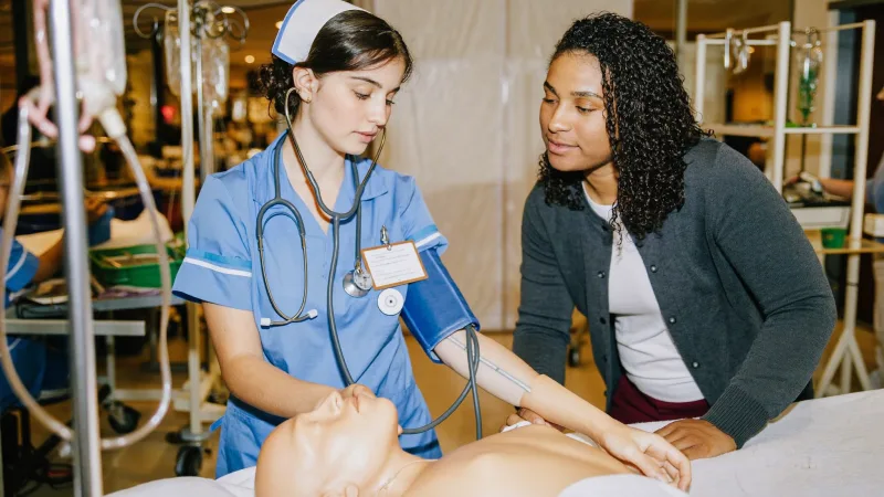 A nursing apprentice practising a clinical skill under supervision in a university simulation suite