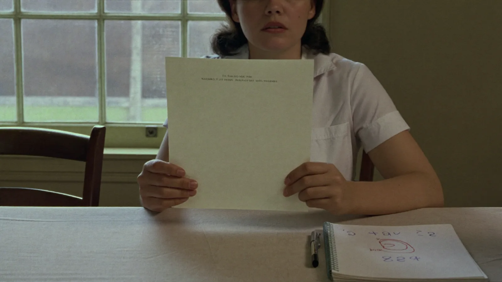 A nurse reading formal correspondence alone at a table, with a union helpline number written on a pad