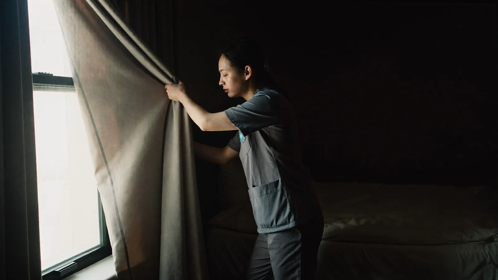 A healthcare worker drawing blackout curtains to sleep during the day after a night shift