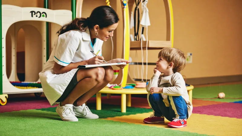 A children’s nurse crouching to talk with a young patient in a colourful hospital play area
