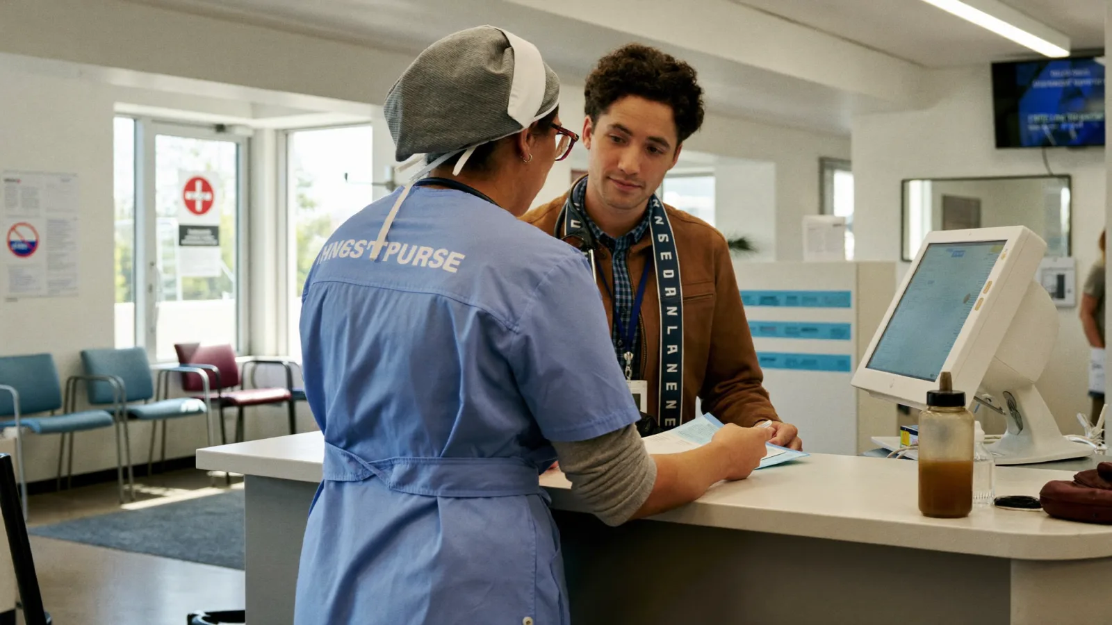 A practice nurse and a colleague talking at the reception desk of a busy general practice