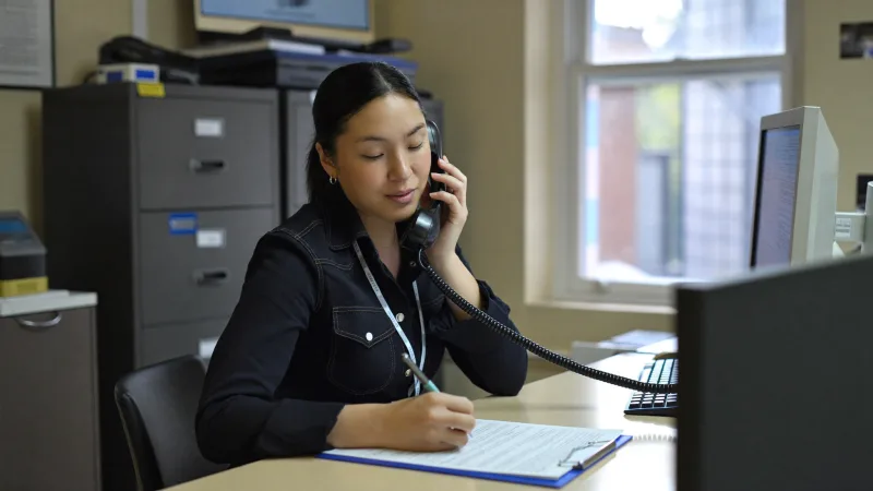 An HR officer on the phone taking notes while checking an employment reference