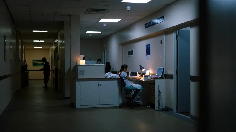 A hospital ward reception desk staffed late at night with corridor lights dimmed